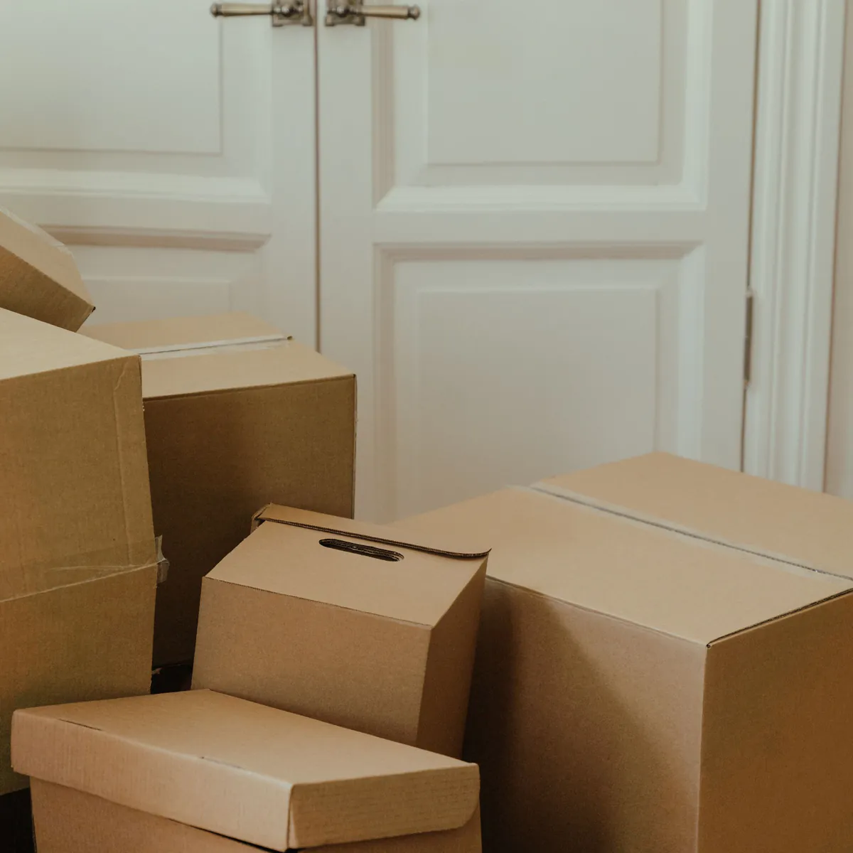 Verhuisdozen naast een witte paneeldeur in de hal van een woning die wordt ontruimd